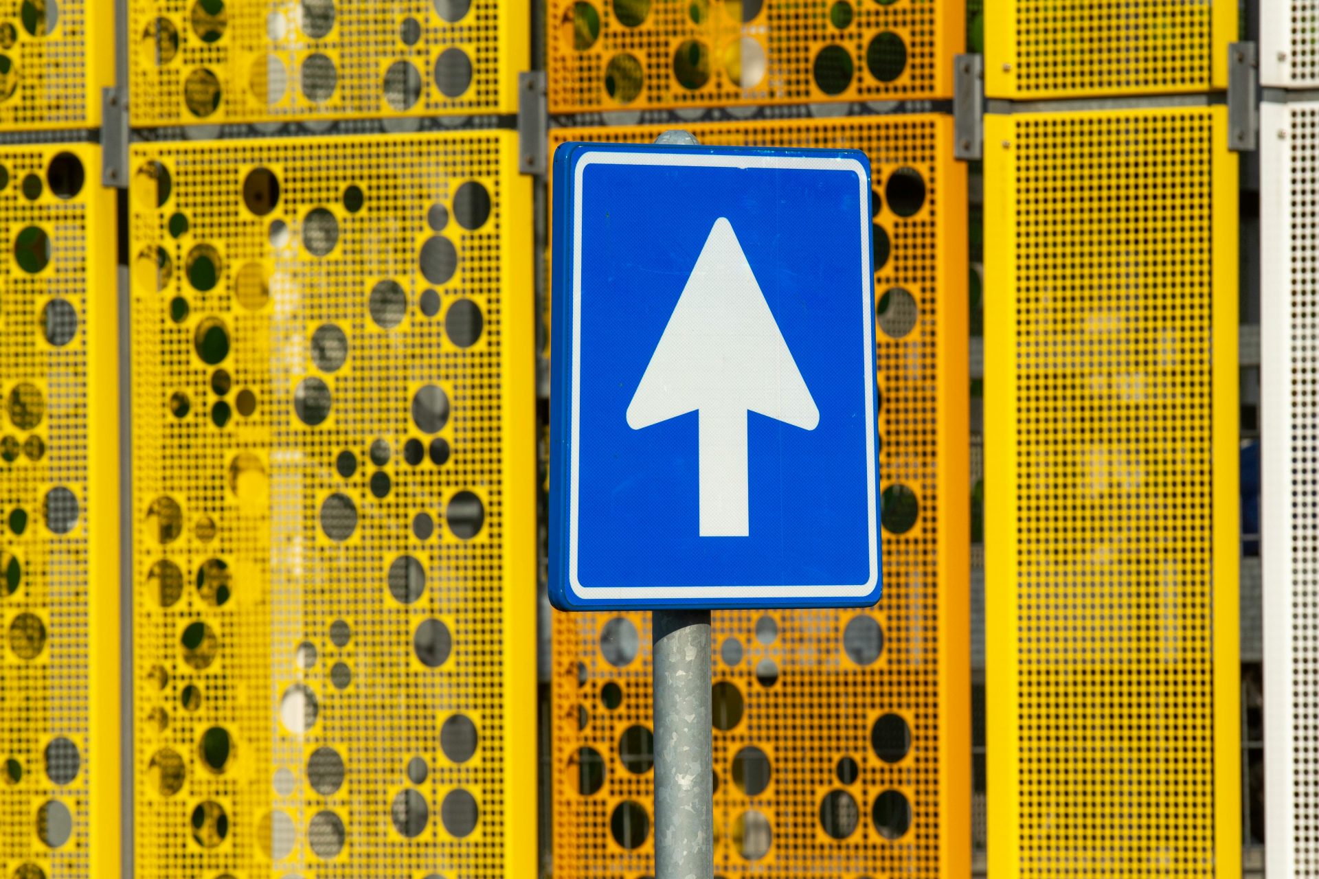 Blue traffic sign with upward arrow on a sunny day, vibrant yellow background.