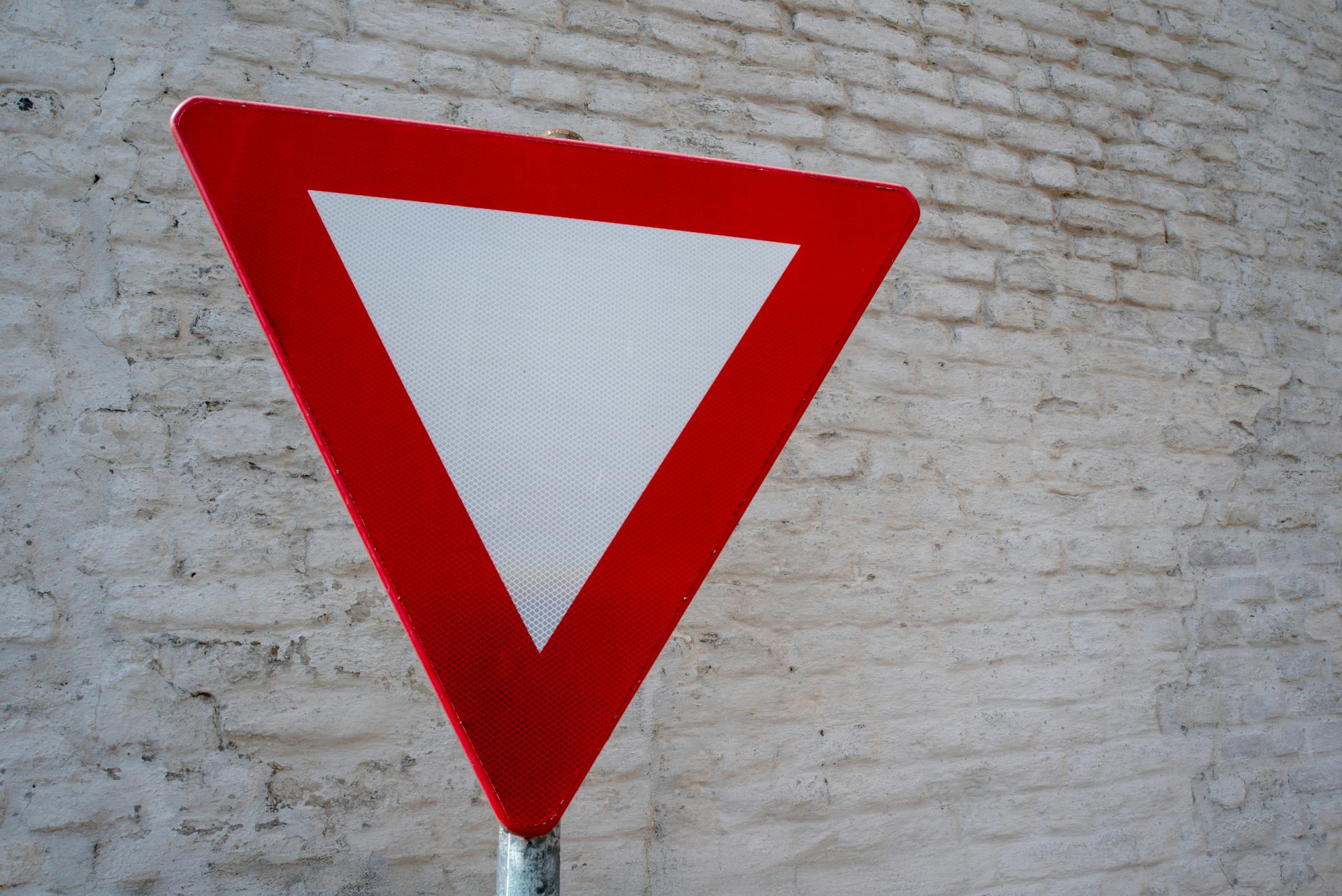 Close-up of red yield traffic sign against a textured white brick wall.