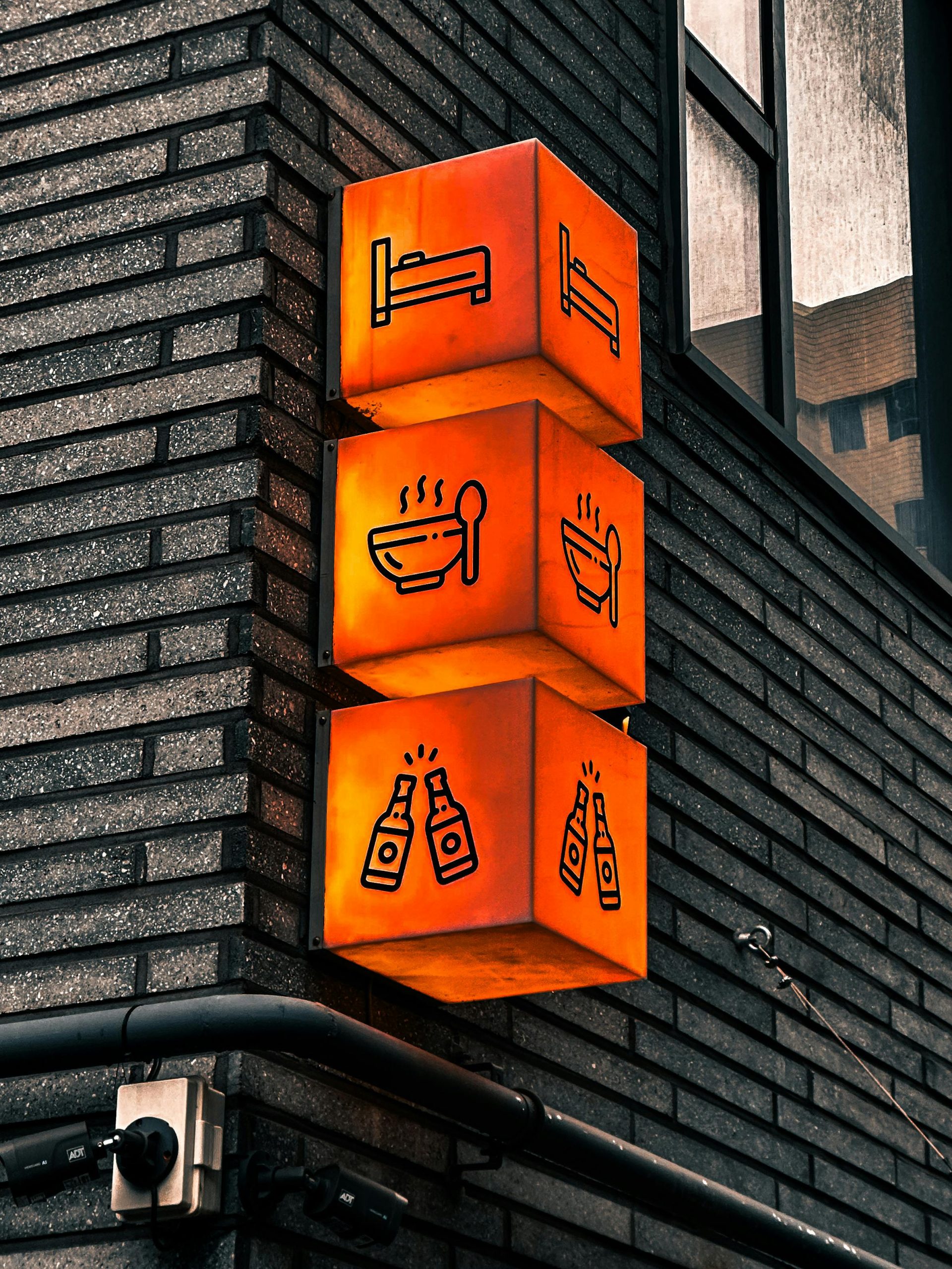 Illuminated cube signs on a brick wall in Seoul showing bed, food, and drink symbols.